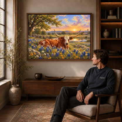 sunset longhorn meadow canvas art in a walnut frame above a console beside a seated man.