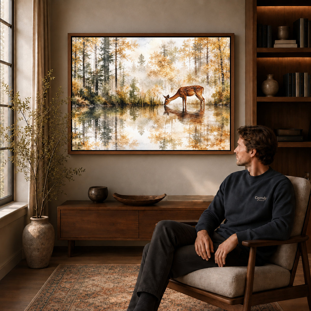 quiet woodland deer canvas art in a walnut frame above a console beside a seated man.