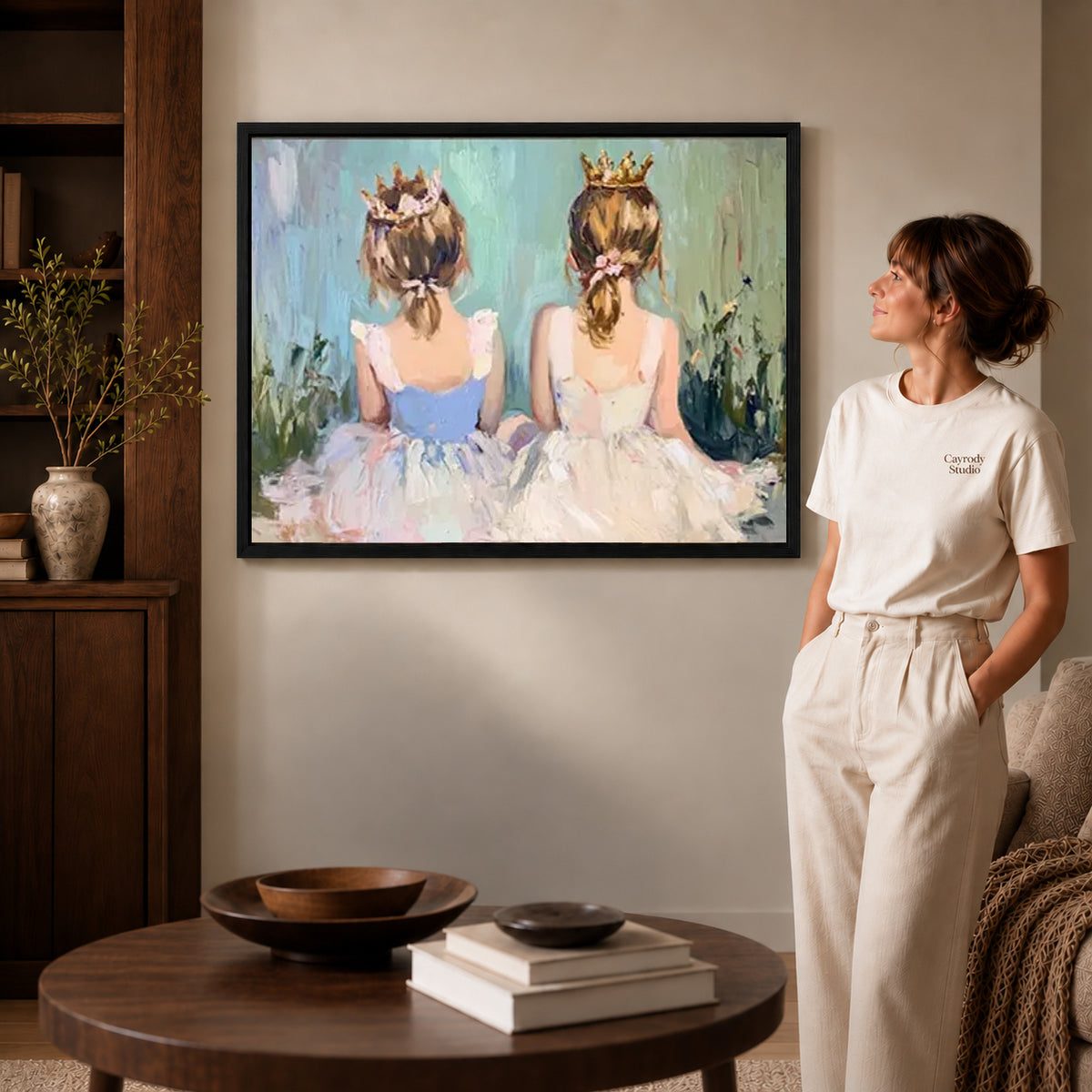 little crown companions canvas art in a black frame beside a woman and round wooden table.