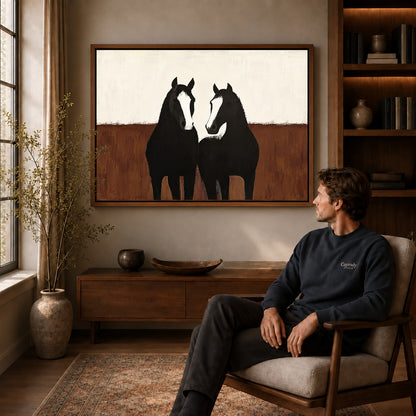 quiet horse companions canvas art in a walnut frame above a console beside a seated man.