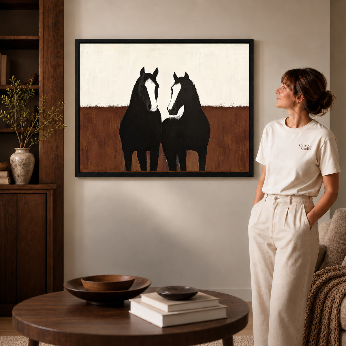 quiet horse companions canvas art in a black frame beside a woman and round wooden table.