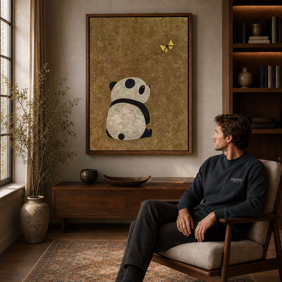panda butterfly moment canvas art in a walnut frame above a console beside a seated man.