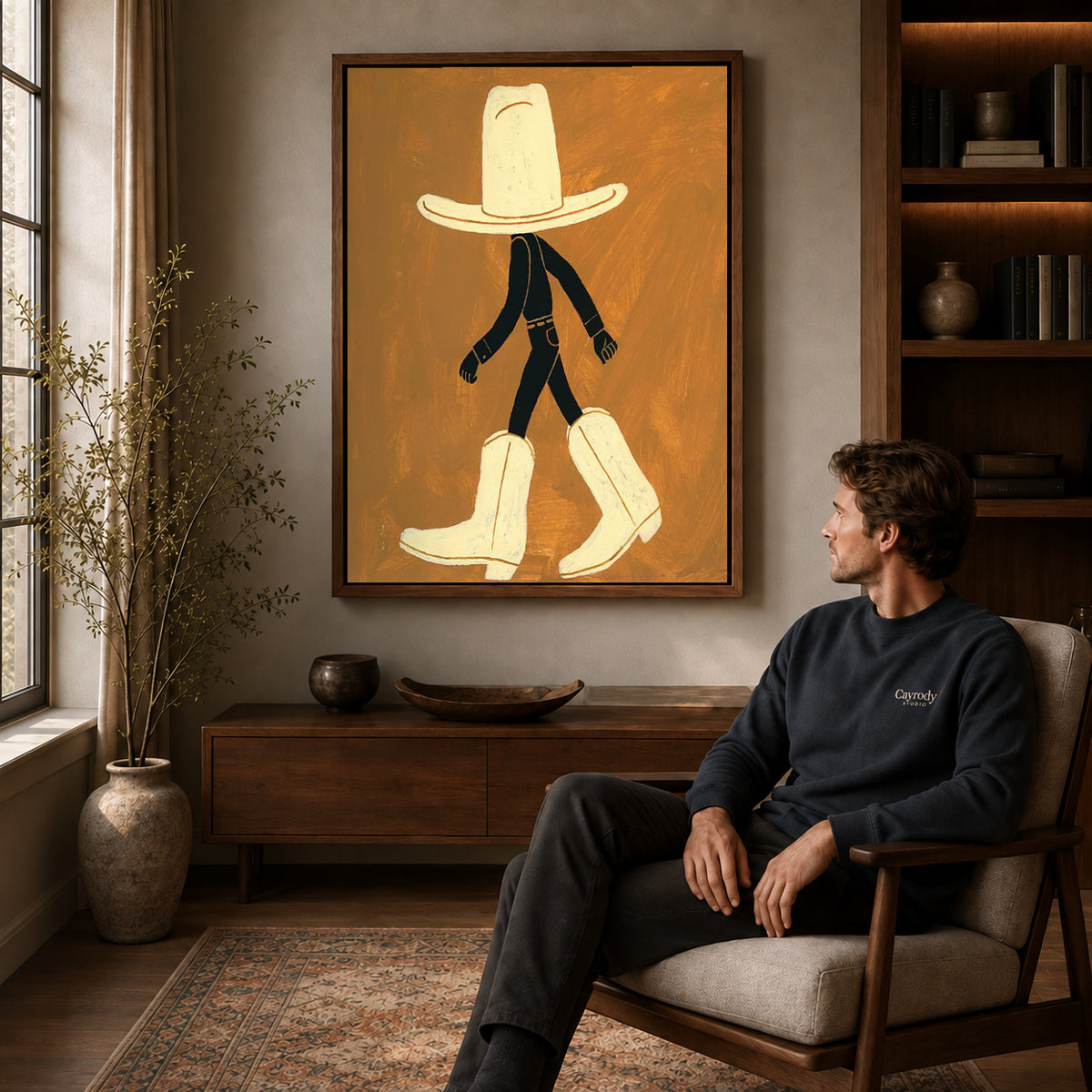 oversized cowboy boots canvas art in a walnut frame above a console beside a seated man.