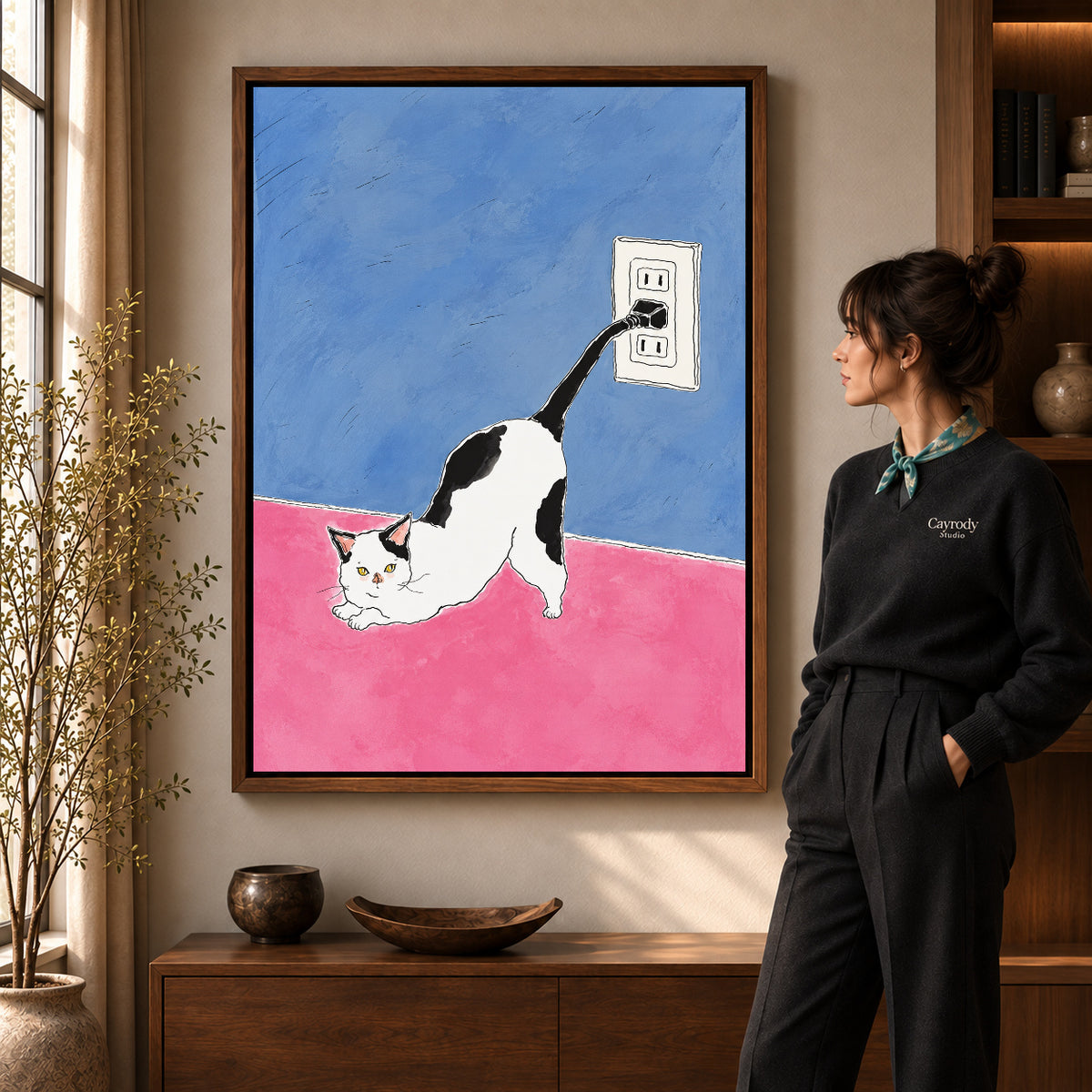 plug tail cat canvas art in a walnut frame beside a standing woman and wooden console.