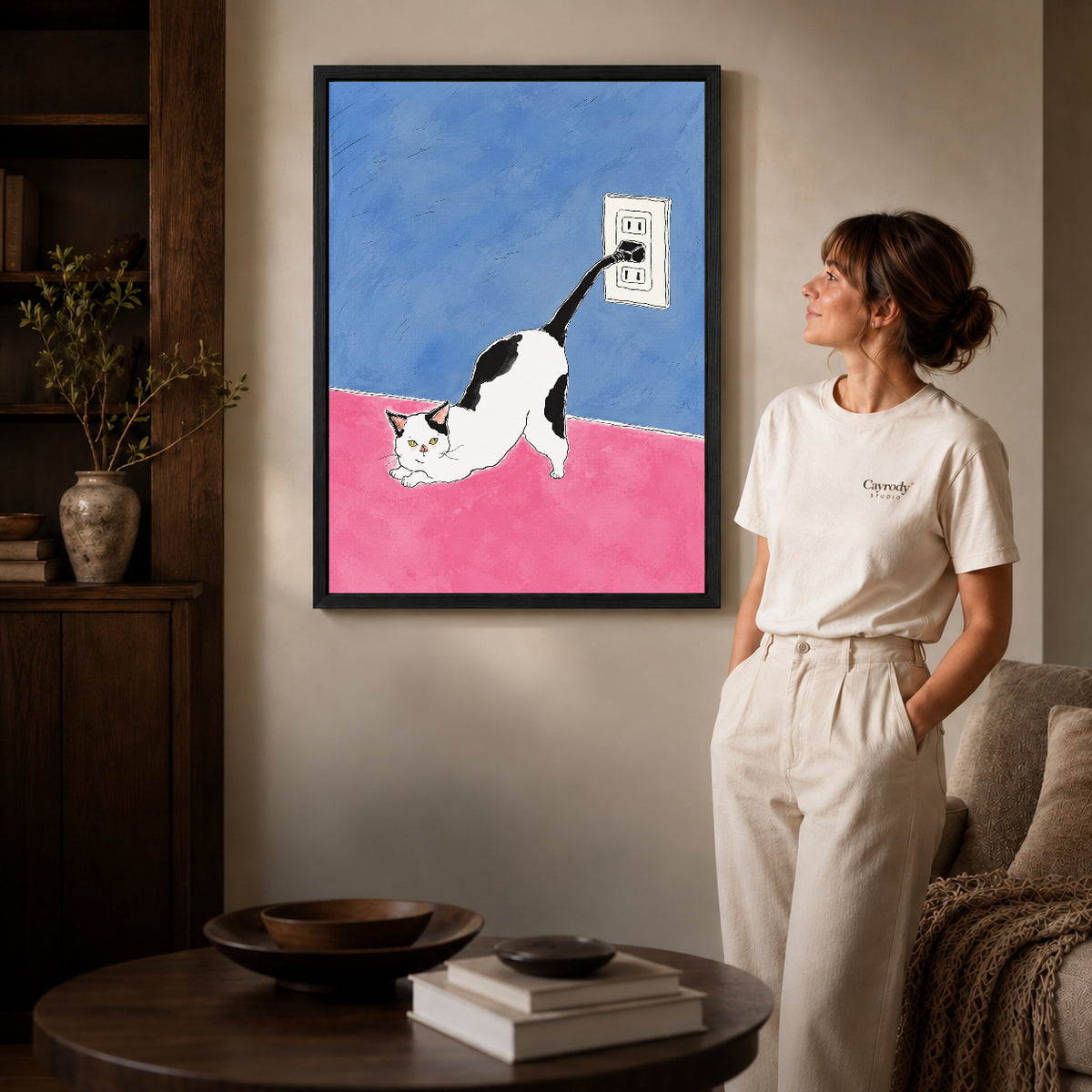 plug tail cat canvas art in a black frame beside a woman and round wooden table.