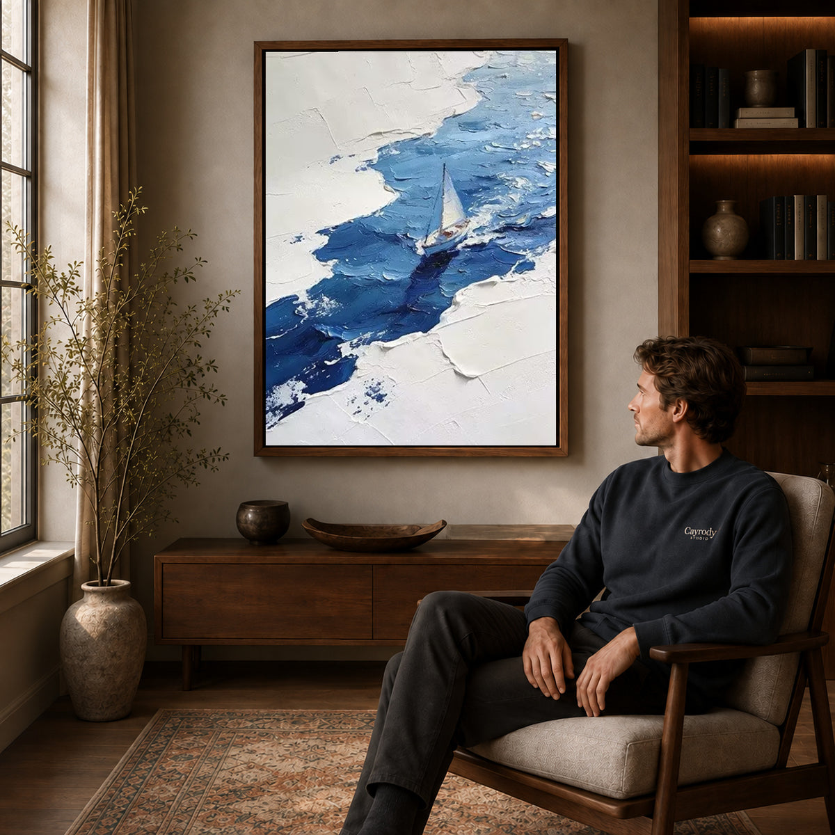 blue impasto sailboat canvas art in a walnut frame above a console beside a seated man.