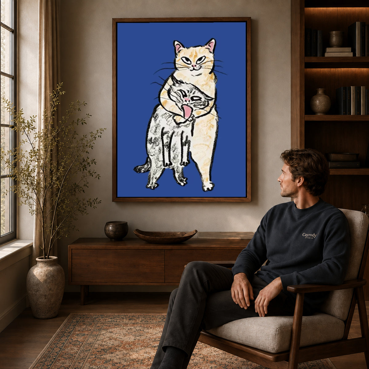 curious cat companions canvas art in a walnut frame above a console beside a seated man.
