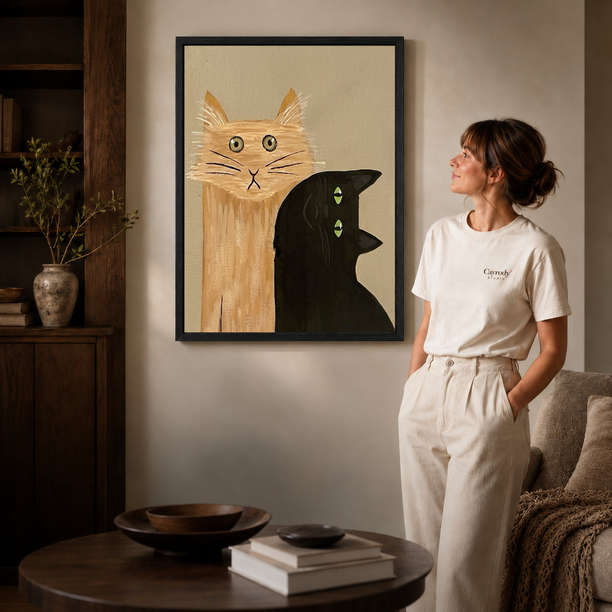 expressive cat gathering canvas art in a black frame beside a woman and round wooden table.
