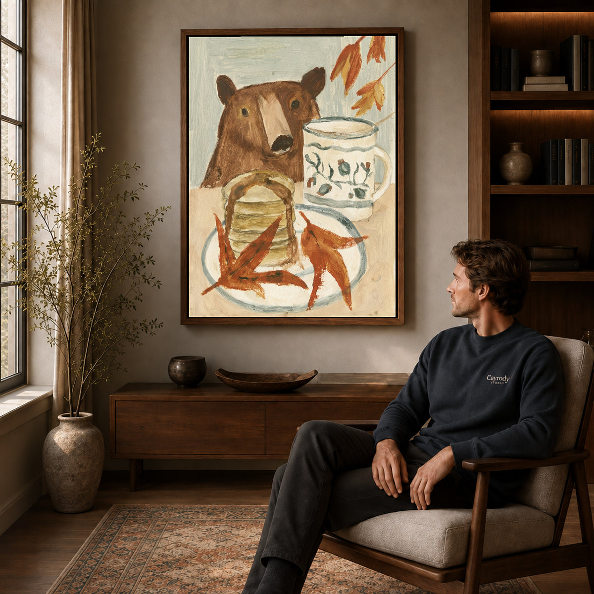 breakfast bear companion canvas art in a walnut frame above a console beside a seated man.