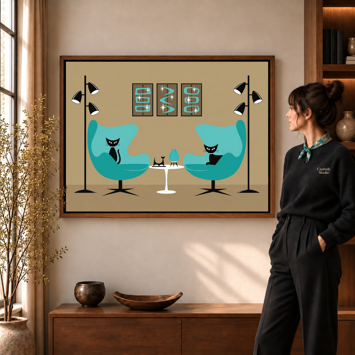 midcentury cat lounge canvas art in a walnut frame beside a standing woman and wooden console.