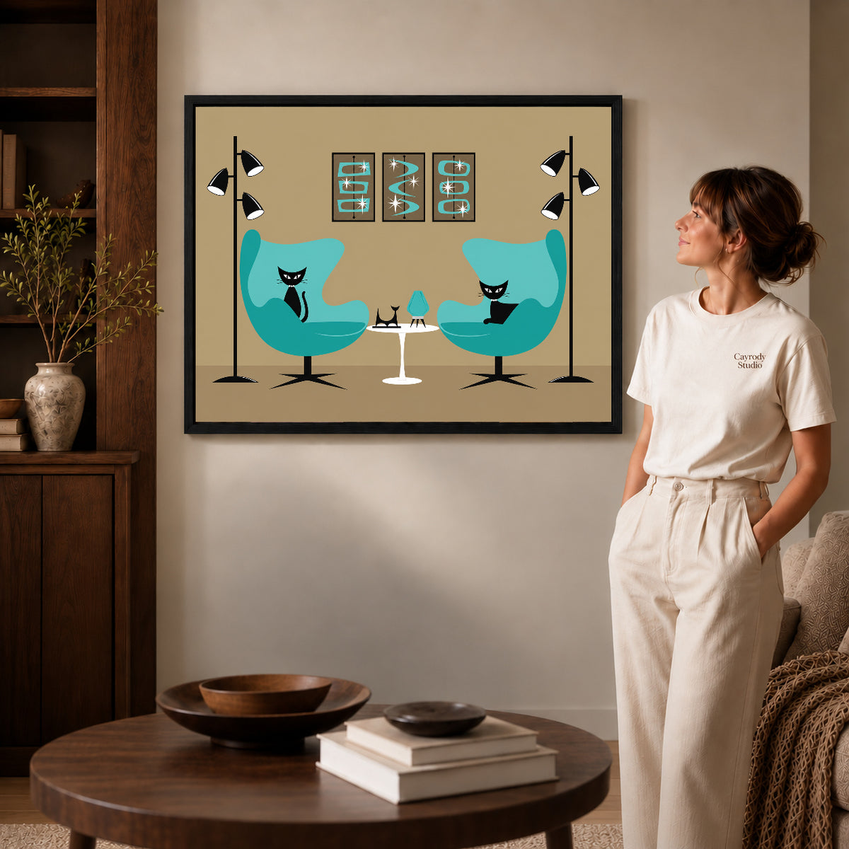midcentury cat lounge canvas art in a black frame beside a woman and round wooden table.
