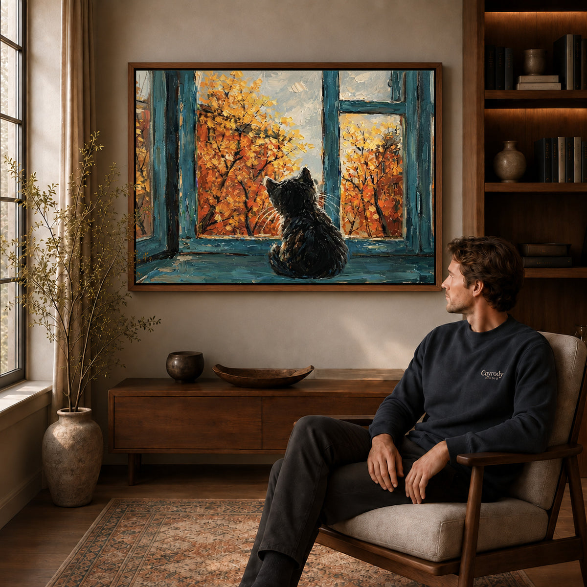 autumn window cat canvas art in a walnut frame above a console beside a seated man.