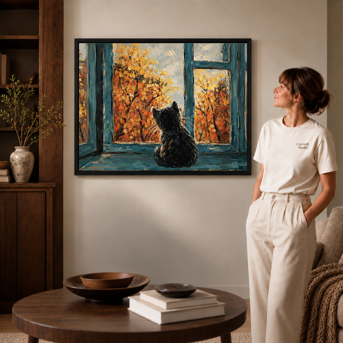 autumn window cat canvas art in a black frame beside a woman and round wooden table.
