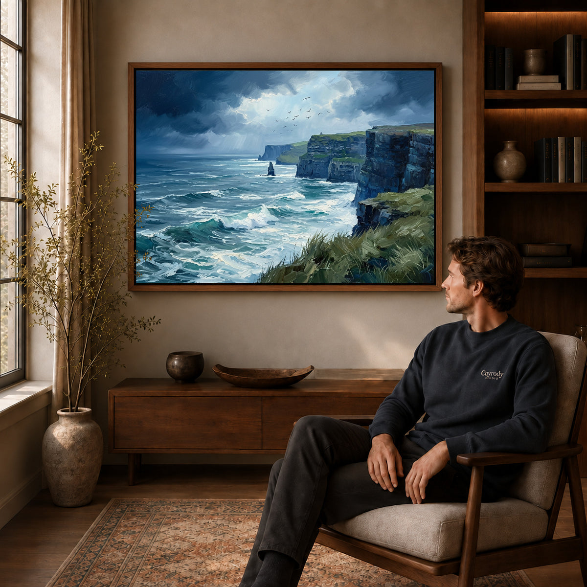wild coastal cliffs canvas art in a walnut frame above a console beside a seated man.