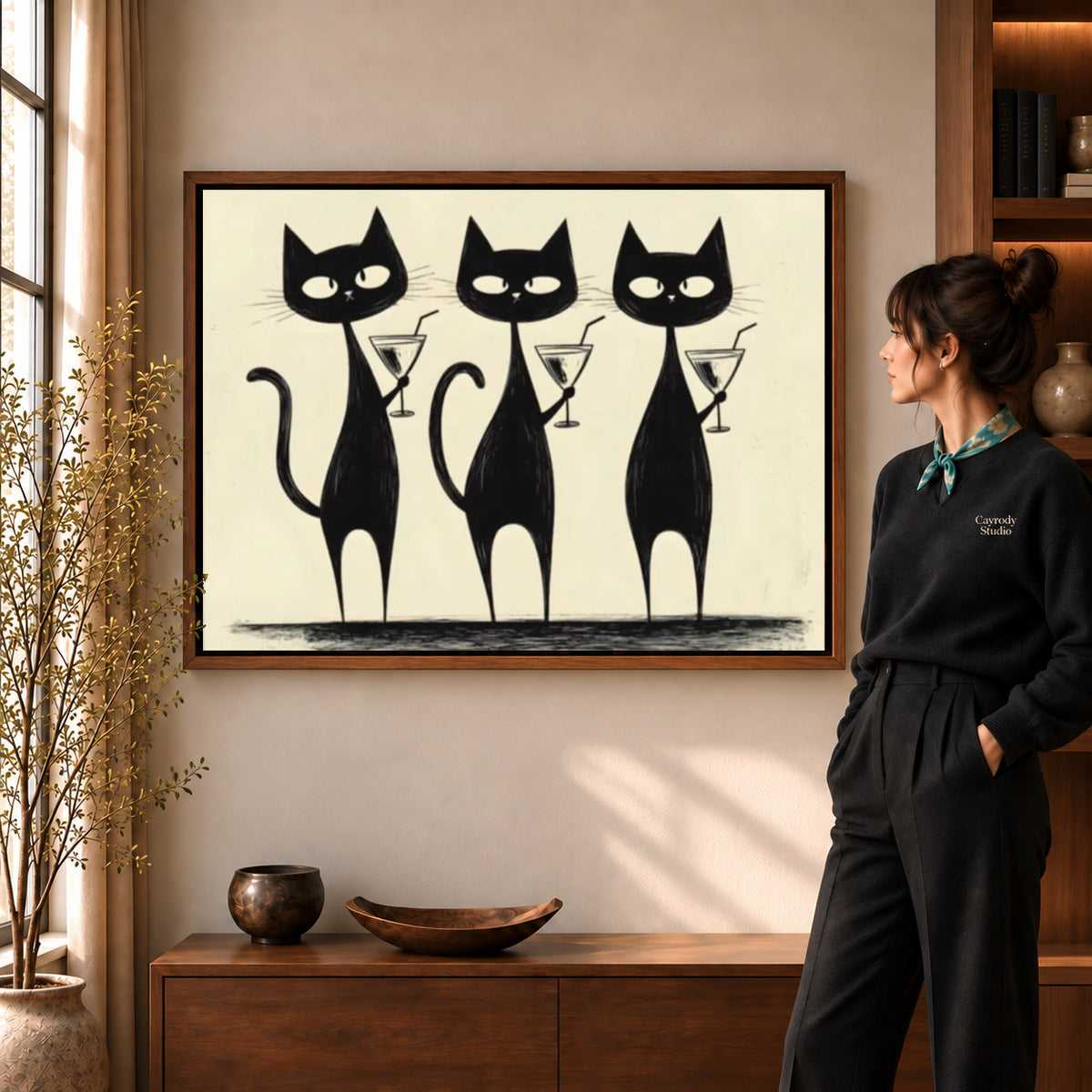 cocktail cat trio canvas art in a walnut frame beside a standing woman and wooden console.