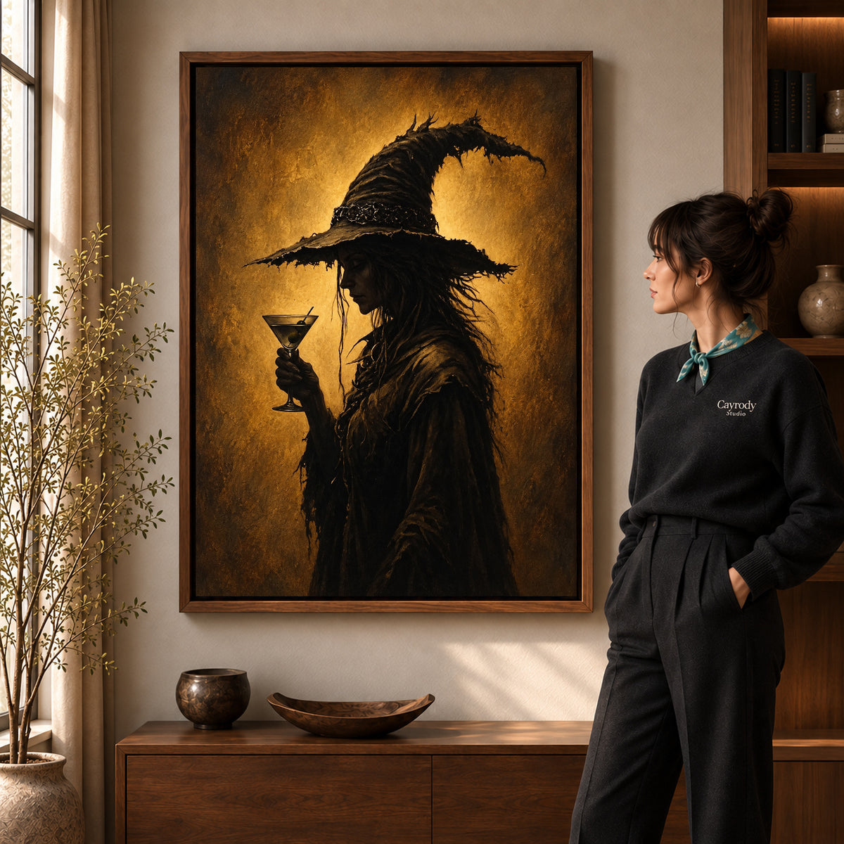 golden twilight witch canvas art in a walnut frame beside a standing woman and wooden console.