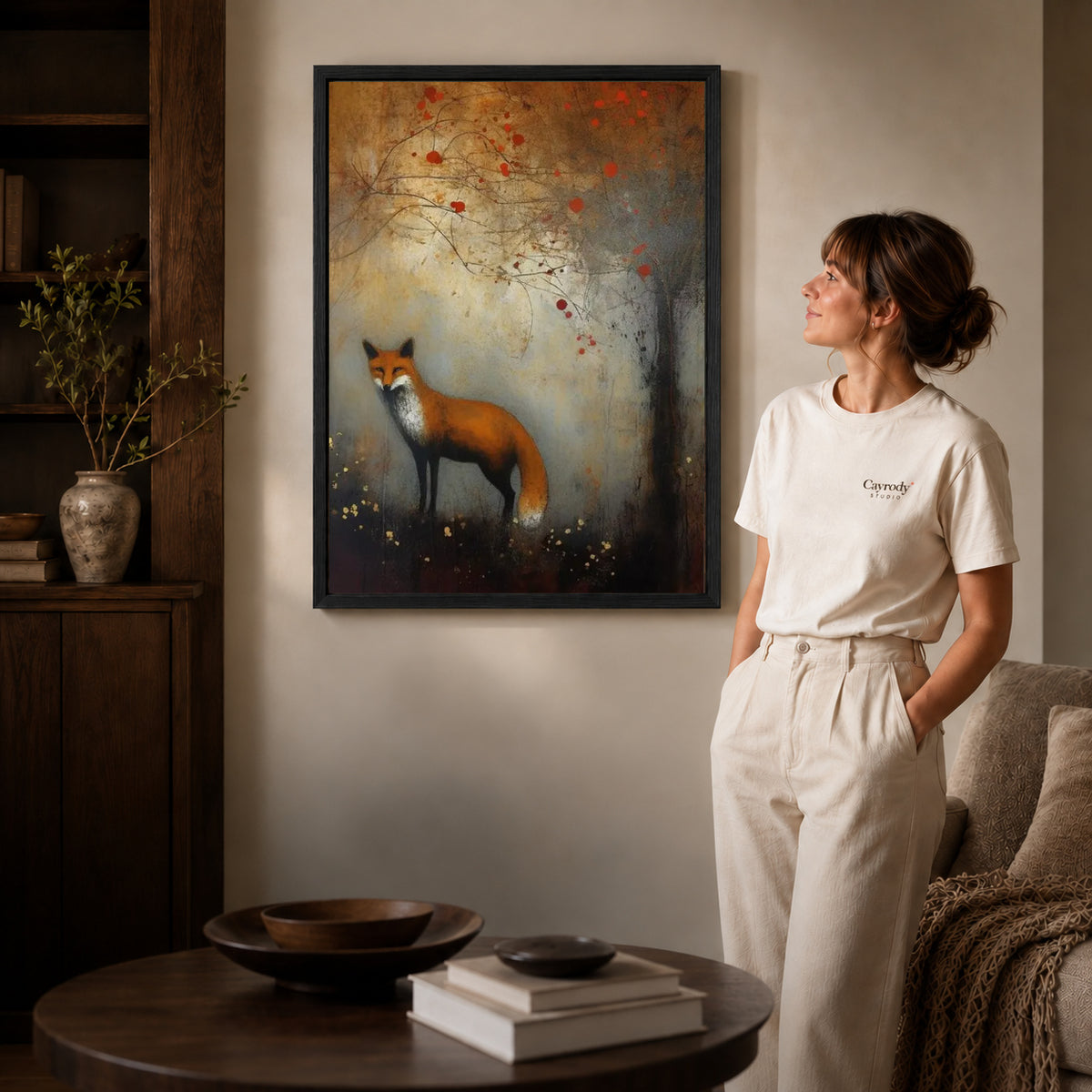 autumn woodland fox canvas art in a black frame beside a woman and round wooden table.