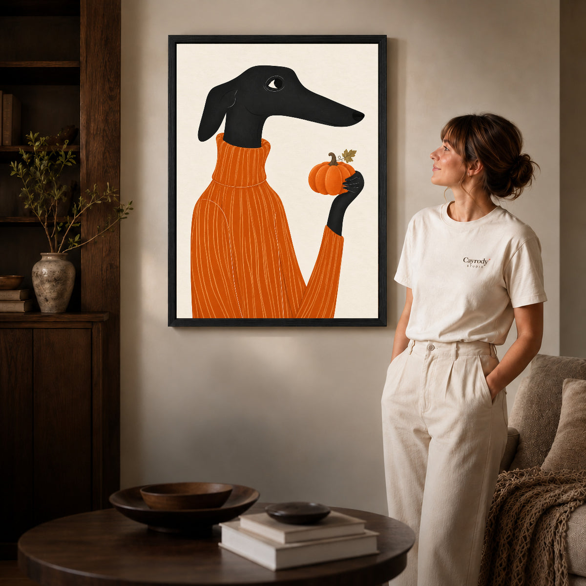 pumpkin sweater dachshund canvas art in a black frame beside a woman and round wooden table.
