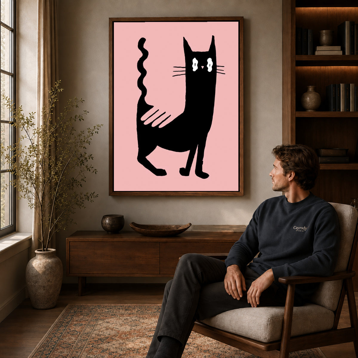 wavy tail cat canvas art in a walnut frame above a console beside a seated man.