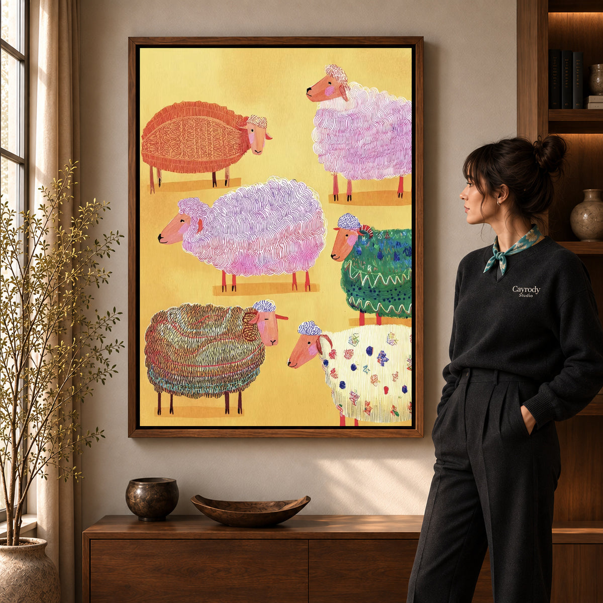 colorful knitted sheep canvas art in a walnut frame beside a standing woman and wooden console.