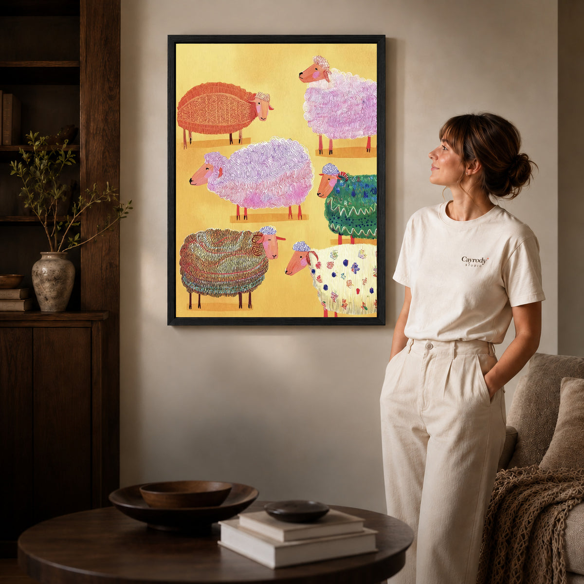 colorful knitted sheep canvas art in a black frame beside a woman and round wooden table.