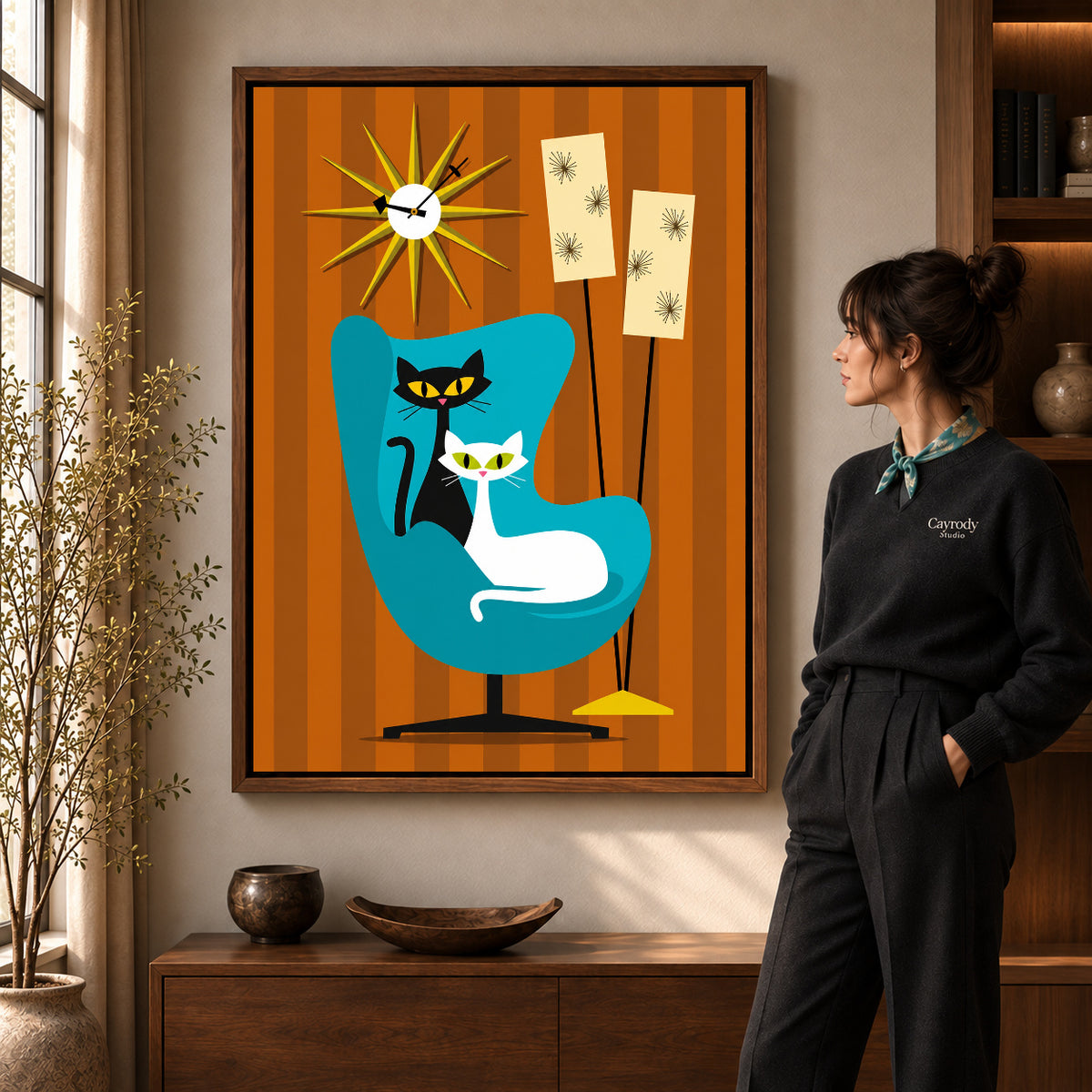 midcentury cat chair canvas art in a walnut frame beside a standing woman and wooden console.