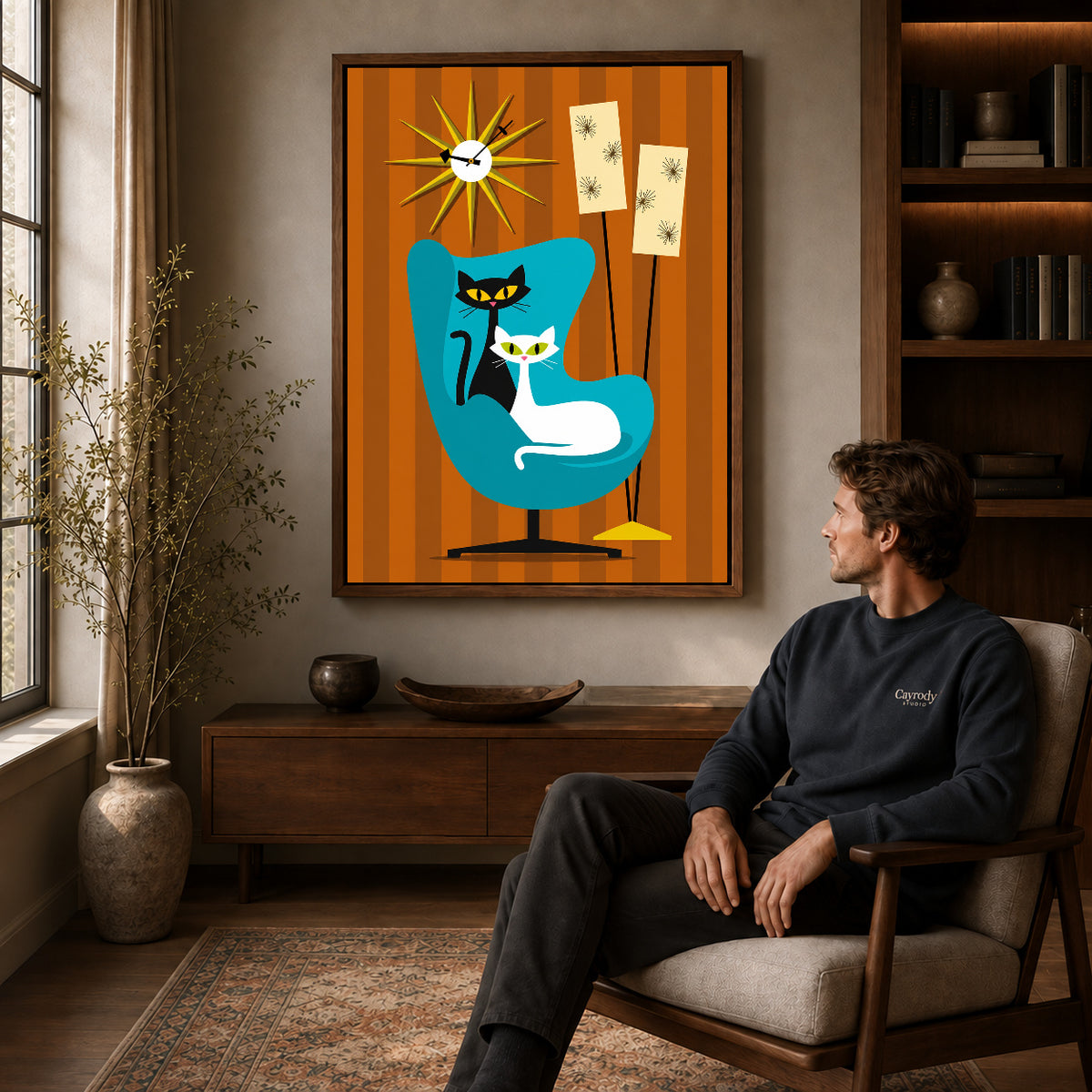 midcentury cat chair canvas art in a walnut frame above a console beside a seated man.
