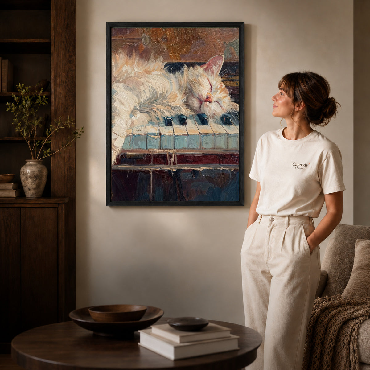 sleepy piano cat canvas art in a black frame beside a woman and round wooden table.