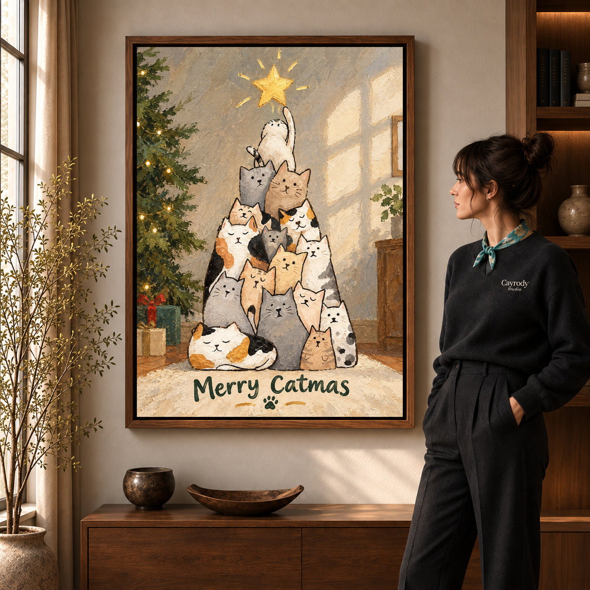 merry catmas gathering canvas art in a walnut frame beside a standing woman and wooden console.