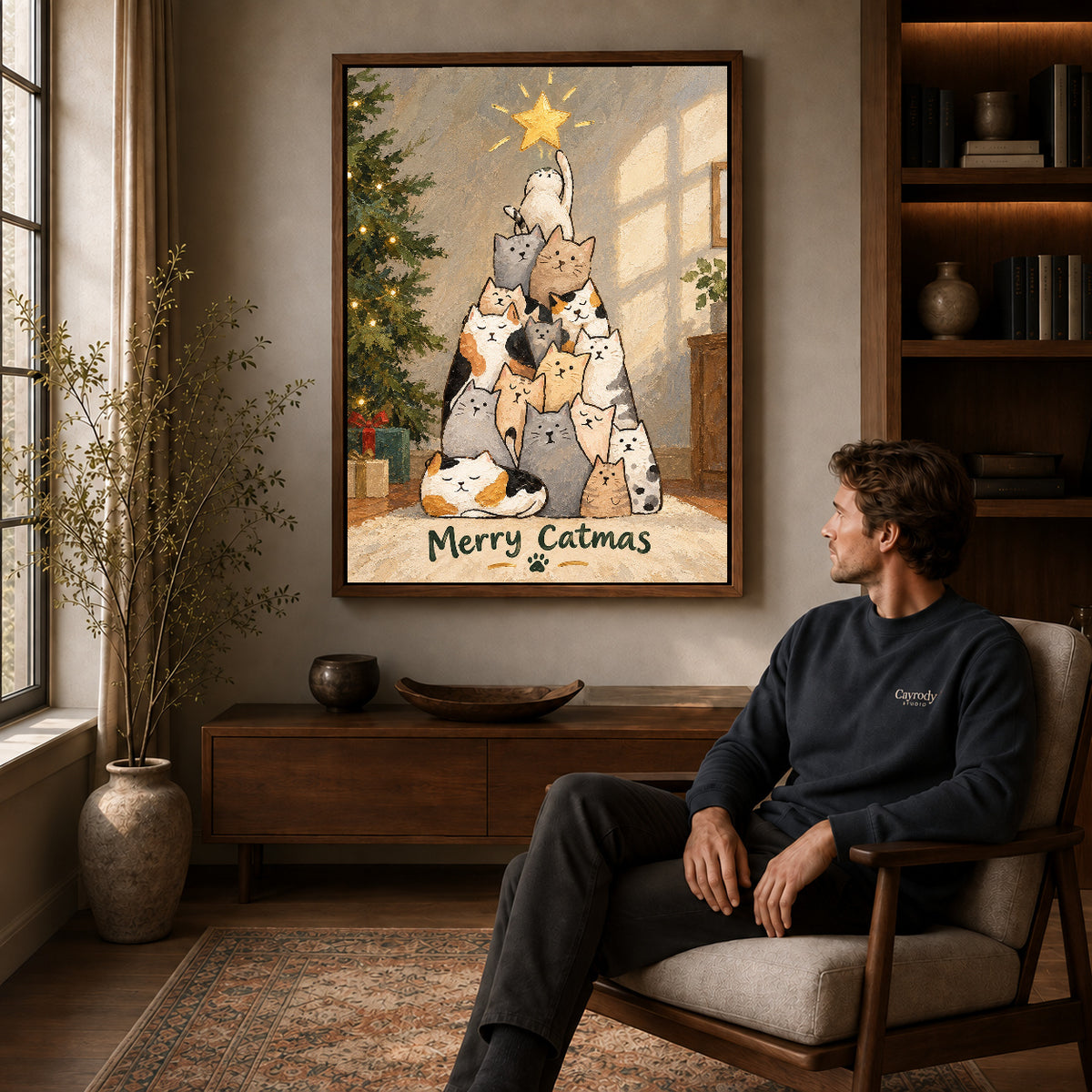 merry catmas gathering canvas art in a walnut frame above a console beside a seated man.