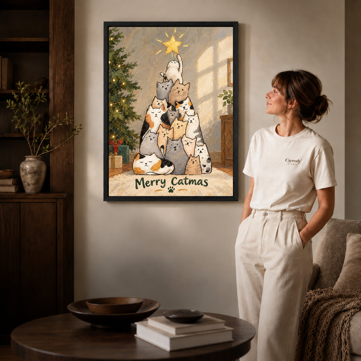 merry catmas gathering canvas art in a black frame beside a woman and round wooden table.