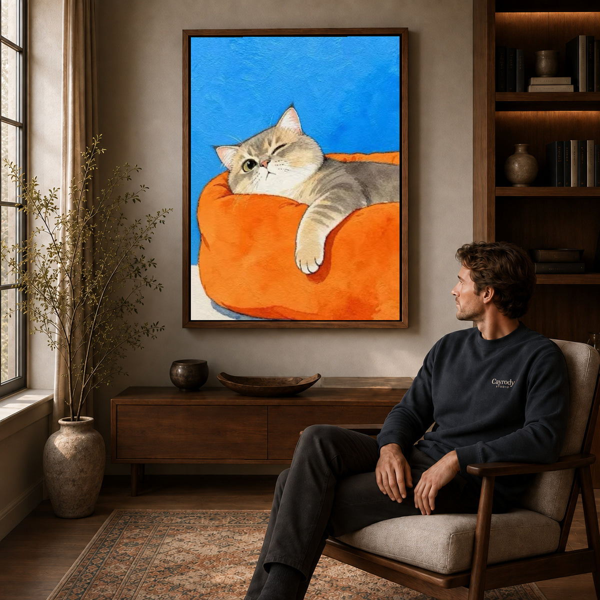 winking armchair cat canvas art in a walnut frame above a console beside a seated man.