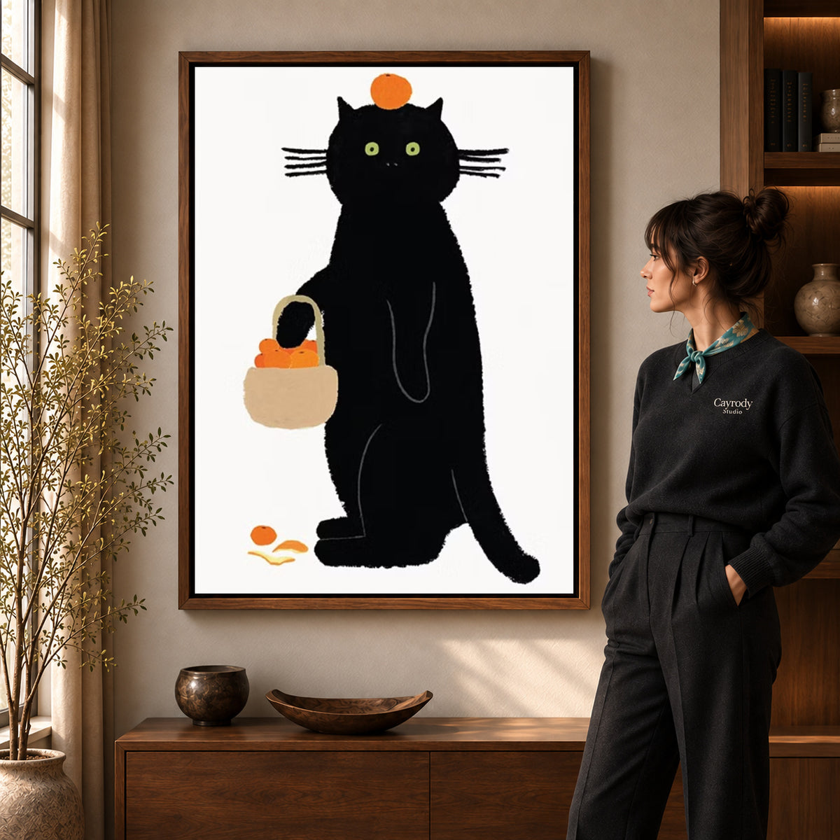 orange basket cat canvas art in a walnut frame beside a standing woman and wooden console.