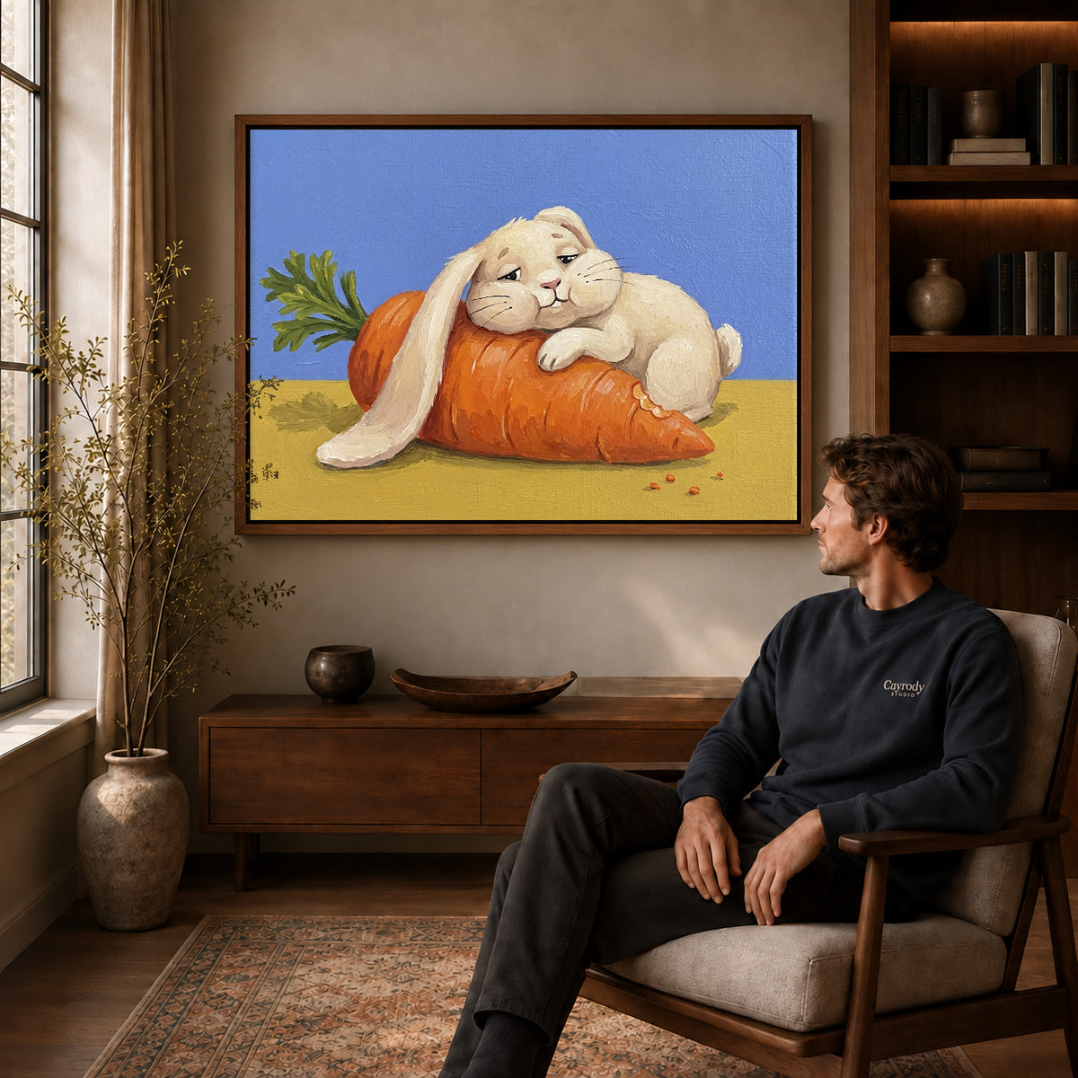 carrot cuddle rabbit canvas art in a walnut frame above a console beside a seated man.