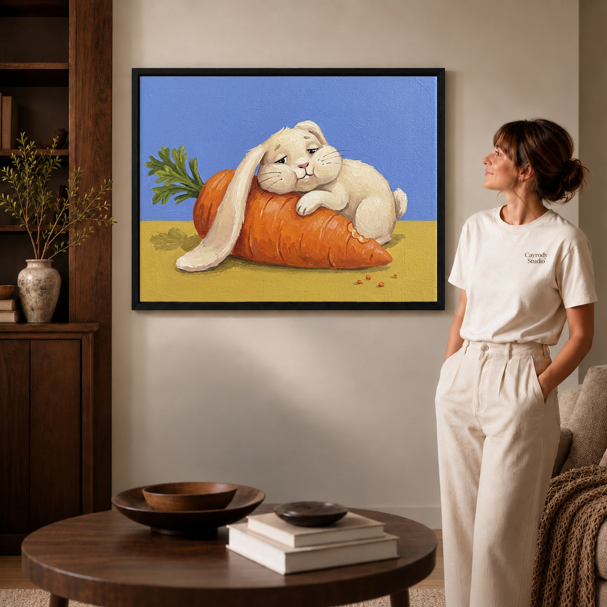 carrot cuddle rabbit canvas art in a black frame beside a woman and round wooden table.