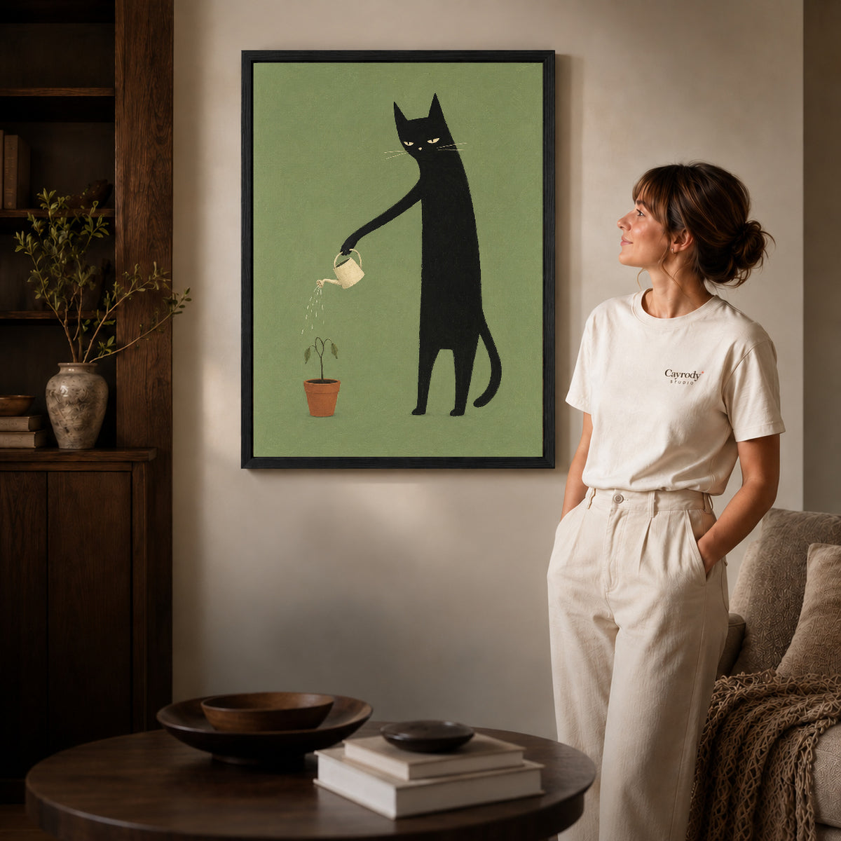 reluctant garden cat canvas art in a black frame beside a woman and round wooden table.