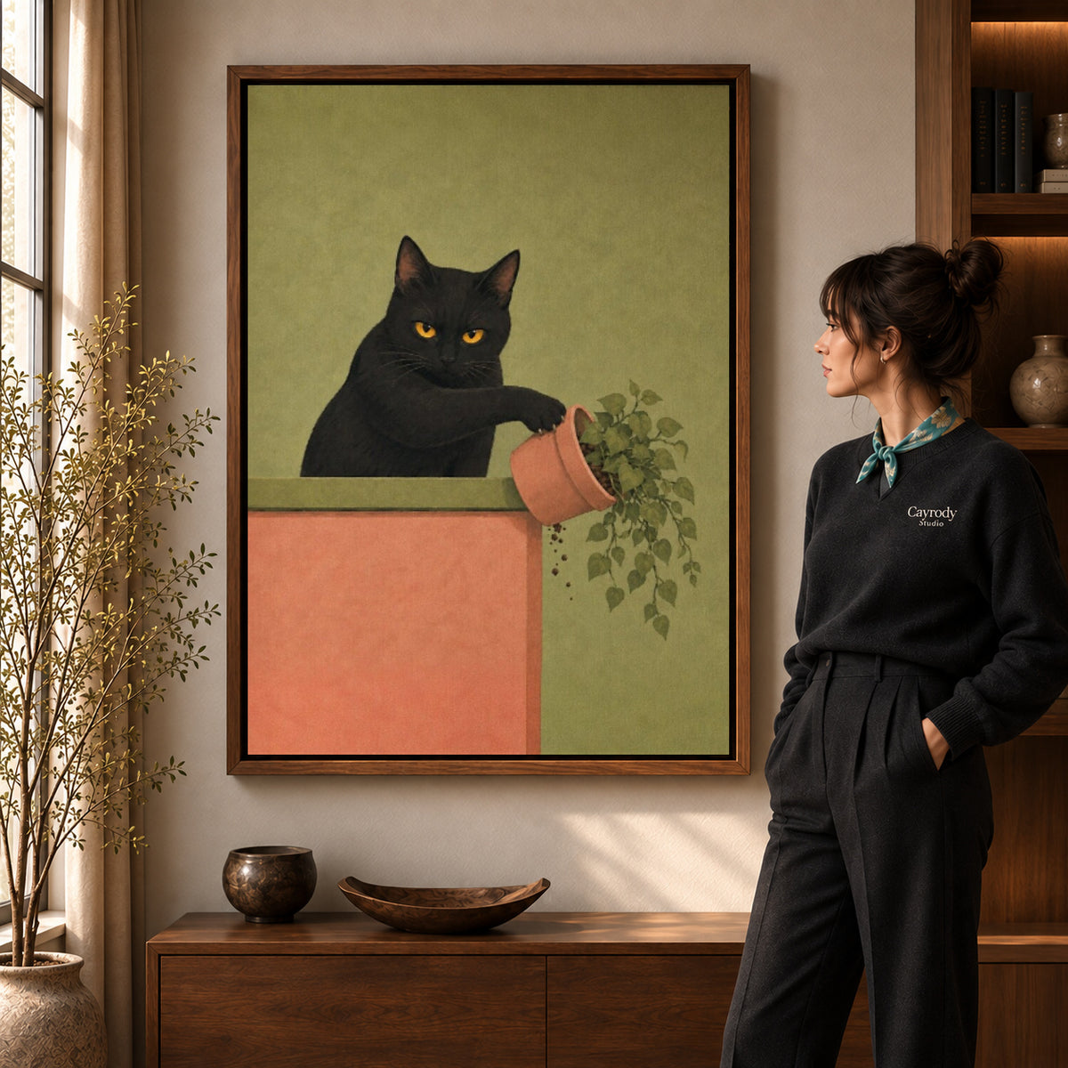 mischievous plant cat canvas art in a walnut frame beside a standing woman and wooden console.