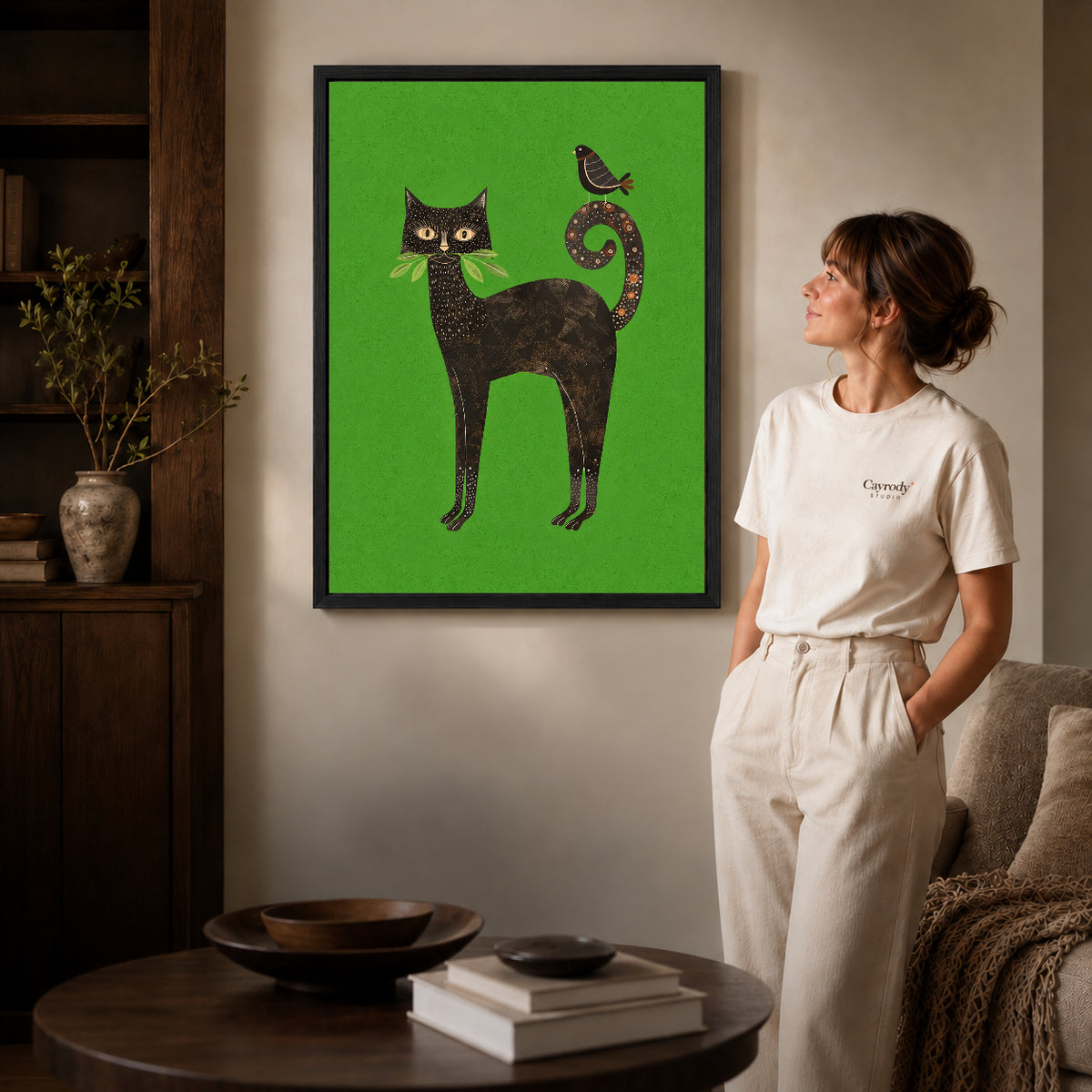 folk garden companions canvas art in a black frame beside a woman and round wooden table.