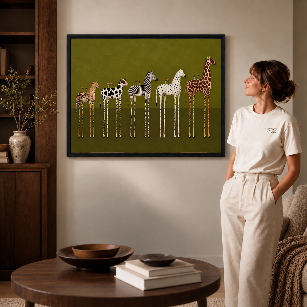 cocktail animal parade canvas art in a black frame beside a woman and round wooden table.