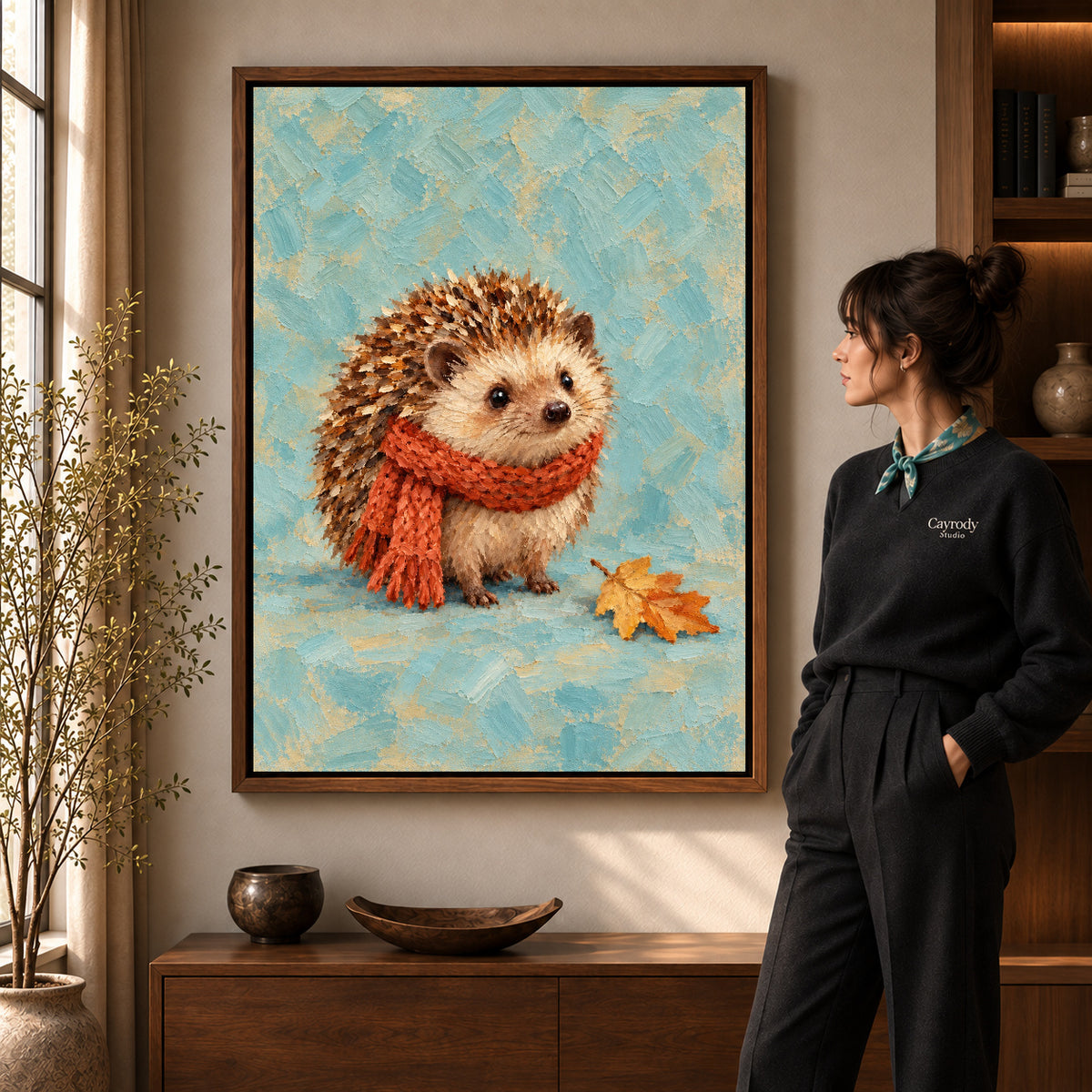 autumn scarf hedgehog canvas art in a walnut frame beside a standing woman and wooden console.