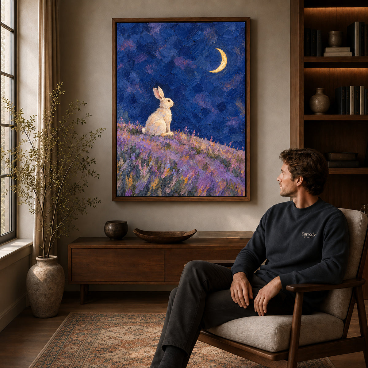 moonlit lavender rabbit canvas art in a walnut frame above a console beside a seated man.