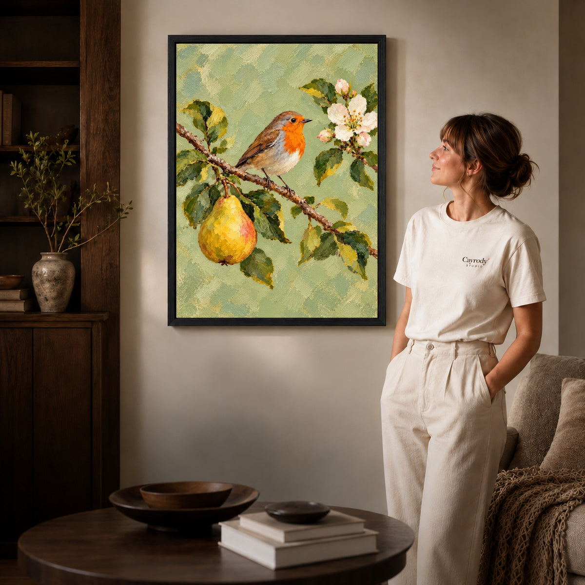 robin pear blossoms canvas art in a black frame beside a woman and round wooden table.