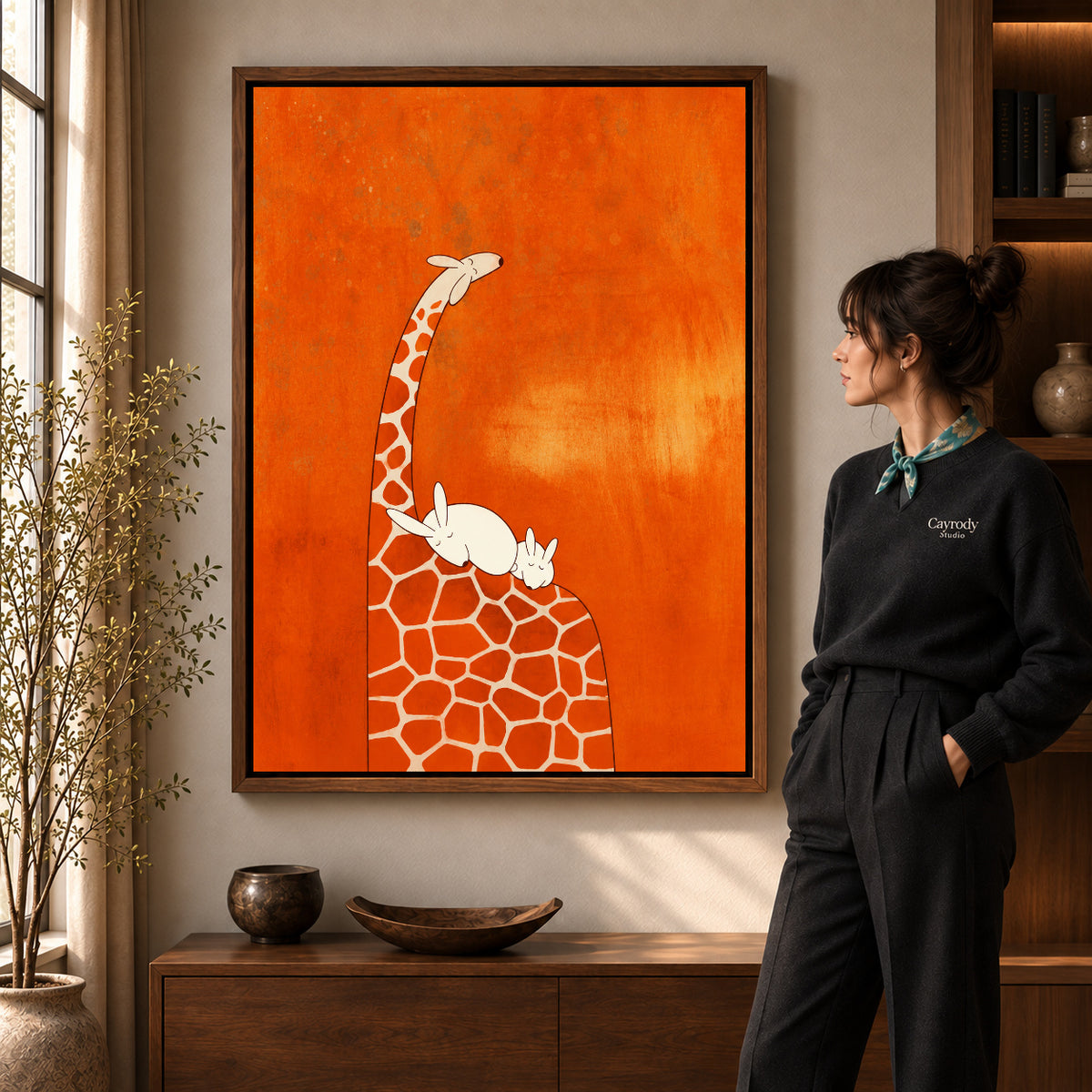 giraffe rabbit rest canvas art in a walnut frame beside a standing woman and wooden console.