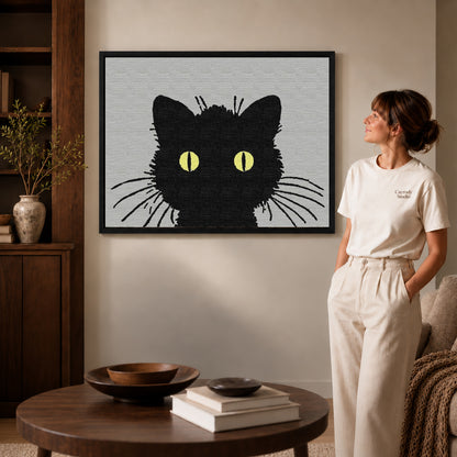 golden eye cat canvas art in a black frame beside a woman and round wooden table.