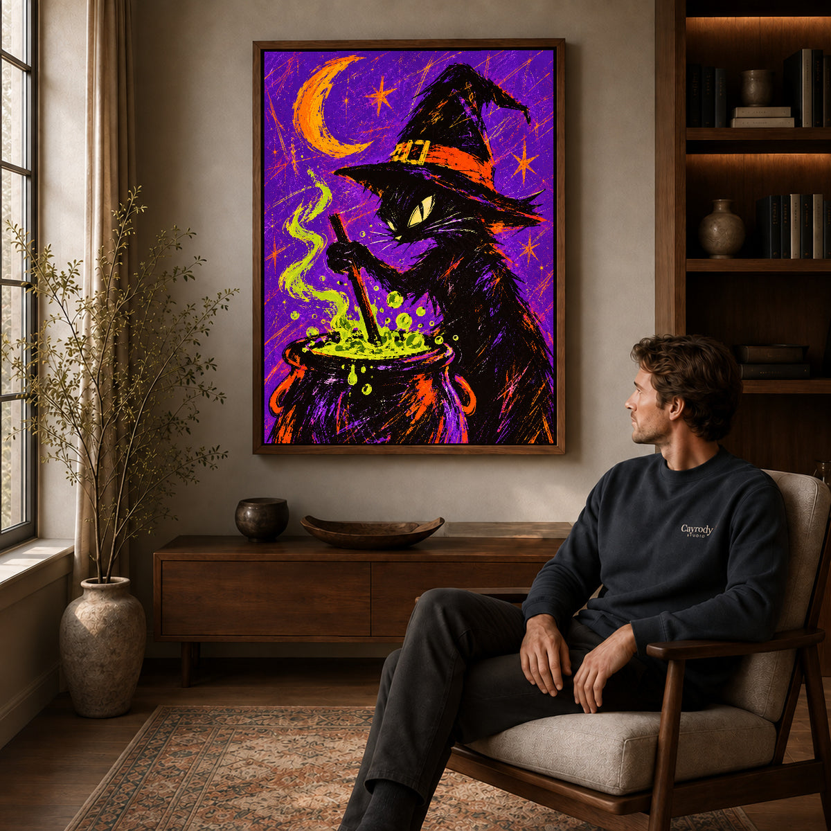 witch cat cauldron canvas art in a walnut frame above a console beside a seated man.