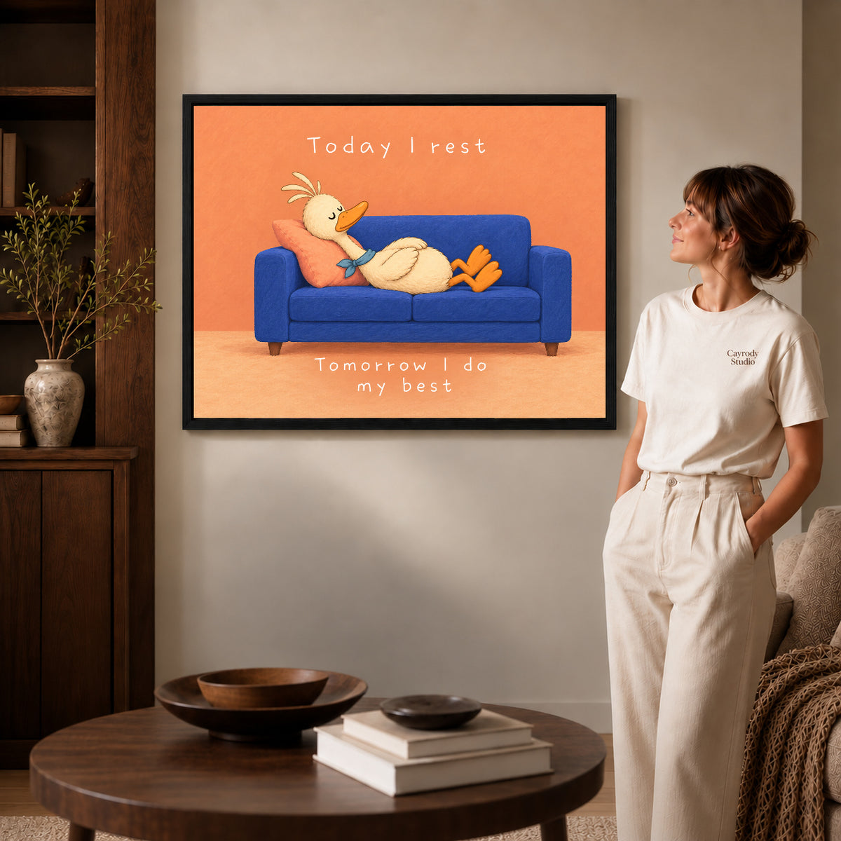 rest day duck canvas art in a black frame beside a woman and round wooden table.