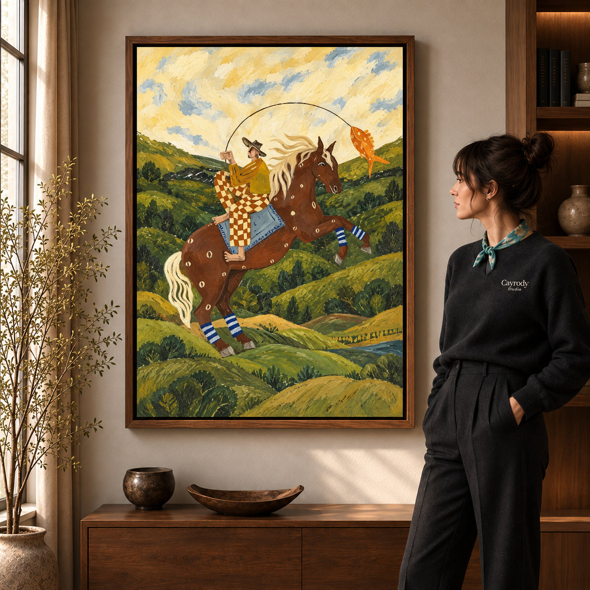 horseback fishing canvas art in a walnut frame beside a standing woman and wooden console.