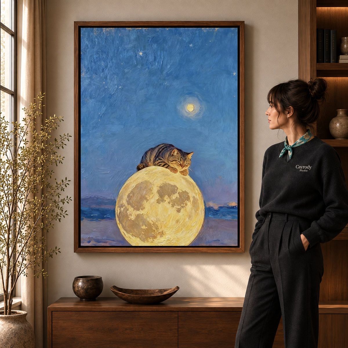moon pillow cat canvas art in a walnut frame beside a standing woman and wooden console.