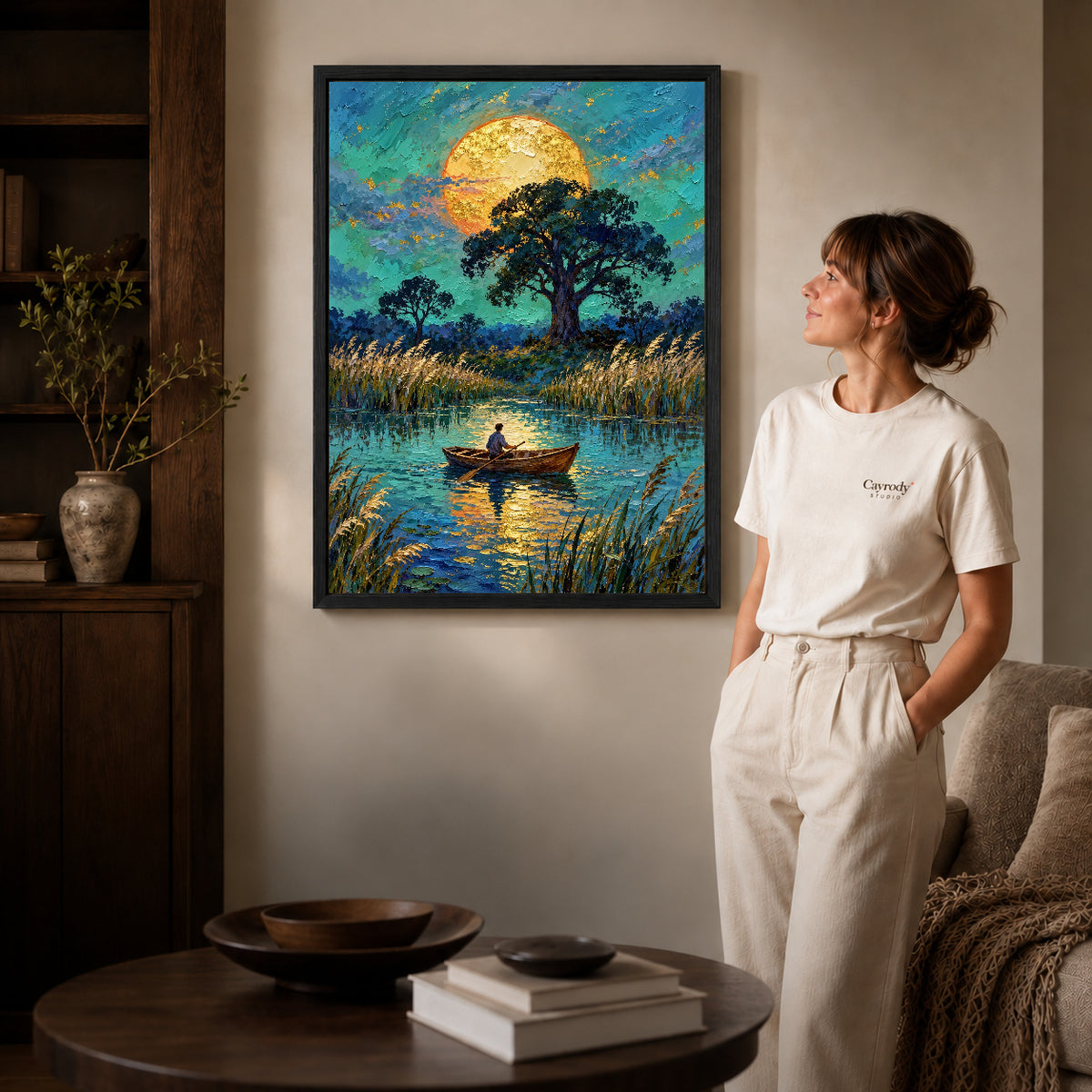 moonlit pond journey canvas art in a black frame beside a woman and round wooden table.