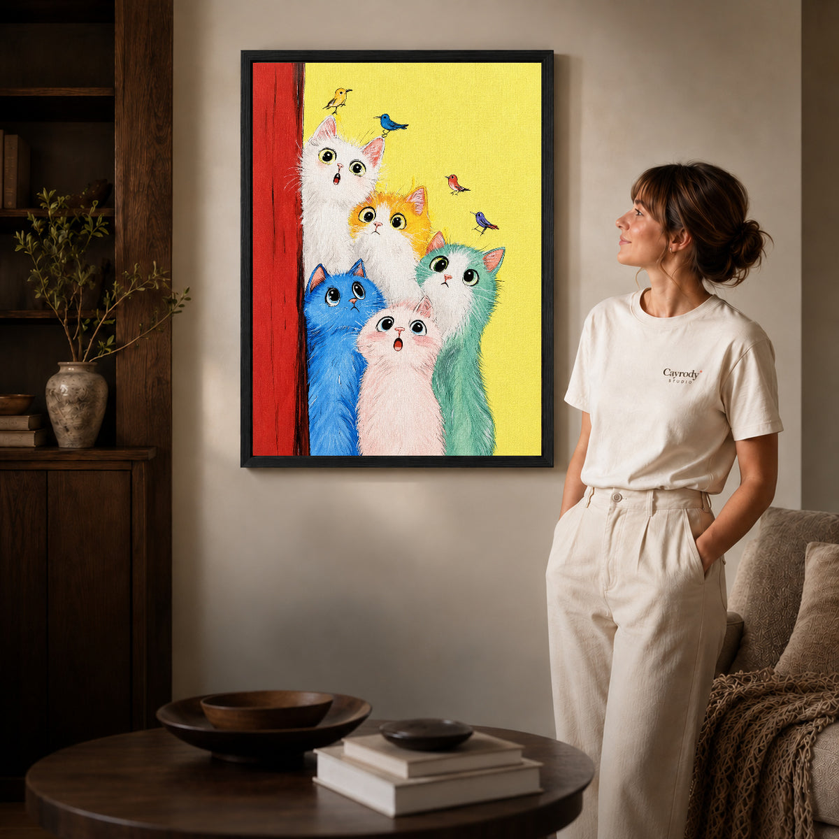 colorful cat chorus canvas art in a black frame beside a woman and round wooden table.